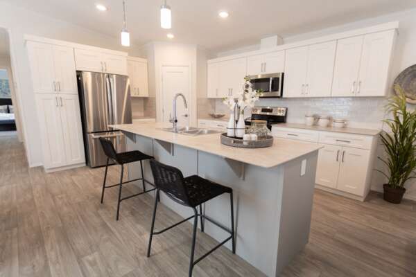 Spacious kitchen in a new manufactured home featuring ample cabinet storage, a built-in microwave, and a contemporary breakfast bar island.